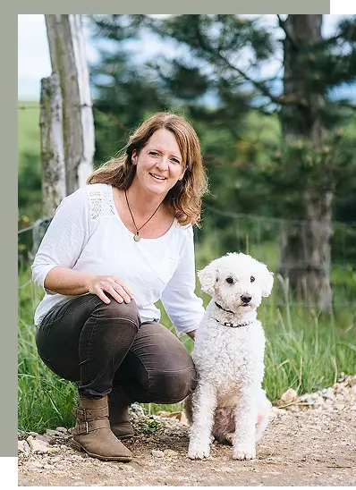 Bild zeigt Kathrin Schneider neben einem weißen Hund auf dem Boden sitzen.